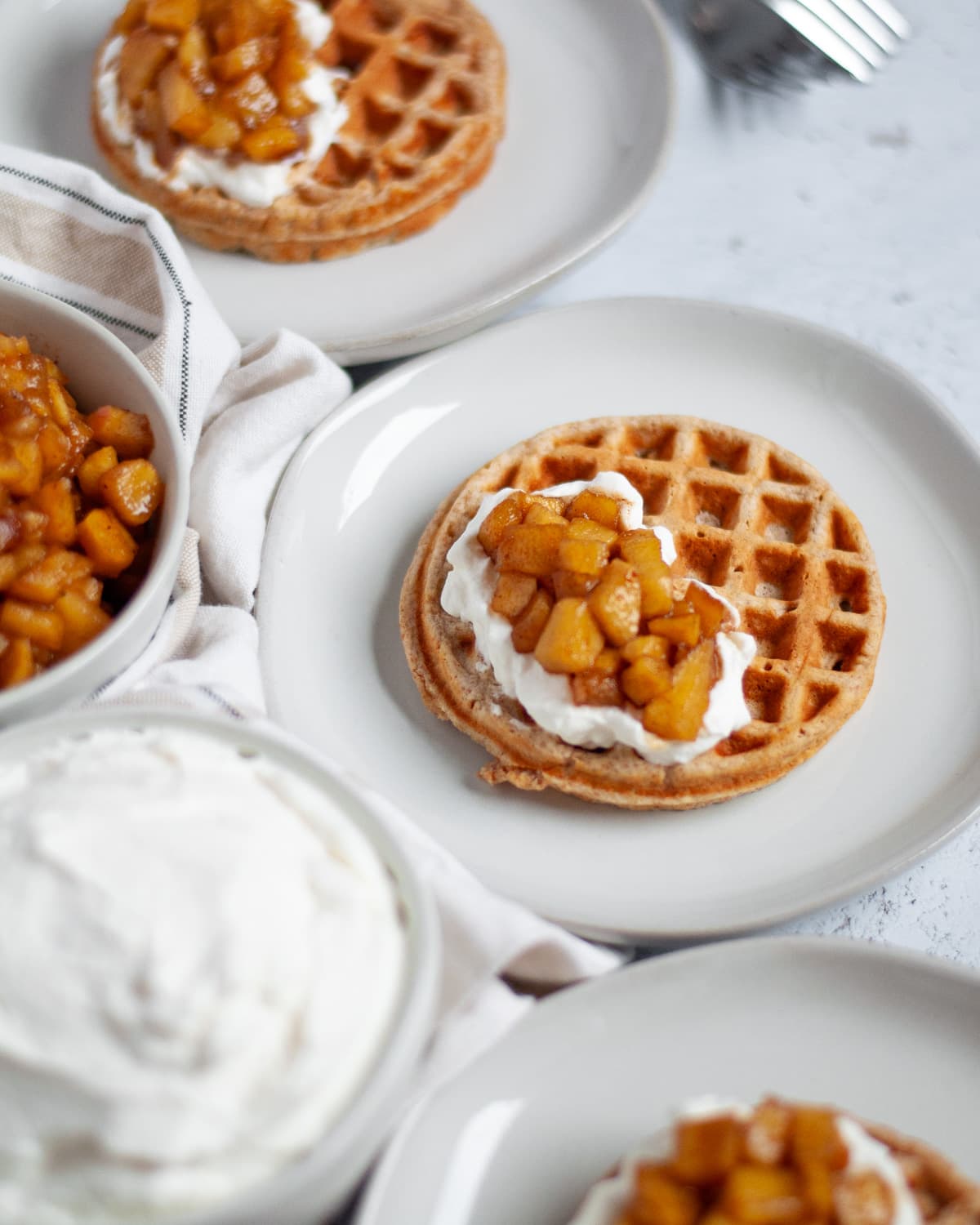 plates of applesauce waffles topped with whipped cream and warm cinnamon apples.
