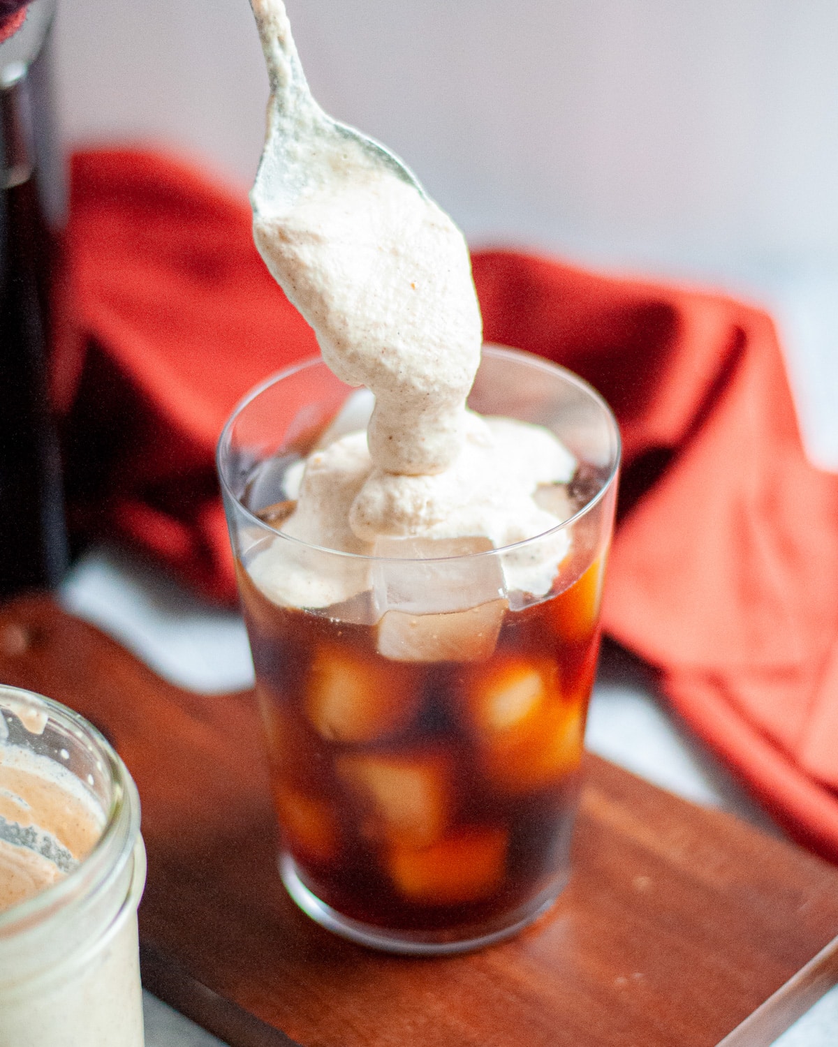 process shot showing pumpkin cream cold foam being spooned onto a tall glass of cold brew.