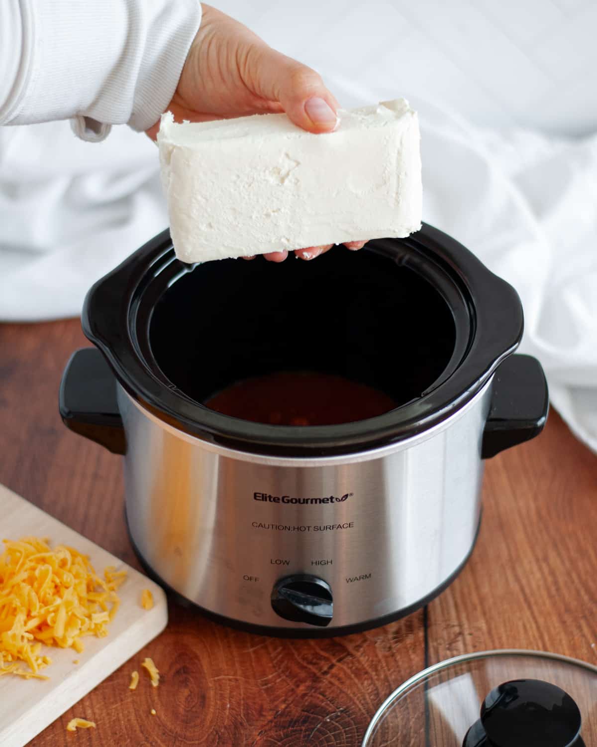 process shot showing how to make 3 ingredient crock pot chili cheese dip. this show shows a block of cream cheese being added on top of chili in a small crock pot.