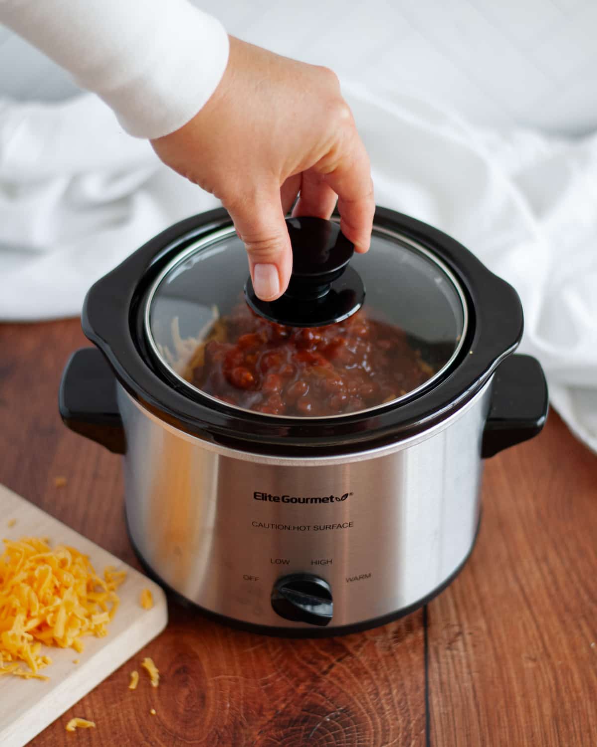 process shot showing how to make 3 ingredient crock pot chili cheese dip. the lid is being added onto a small crockpot filled with ingredients, ready to be turned on.