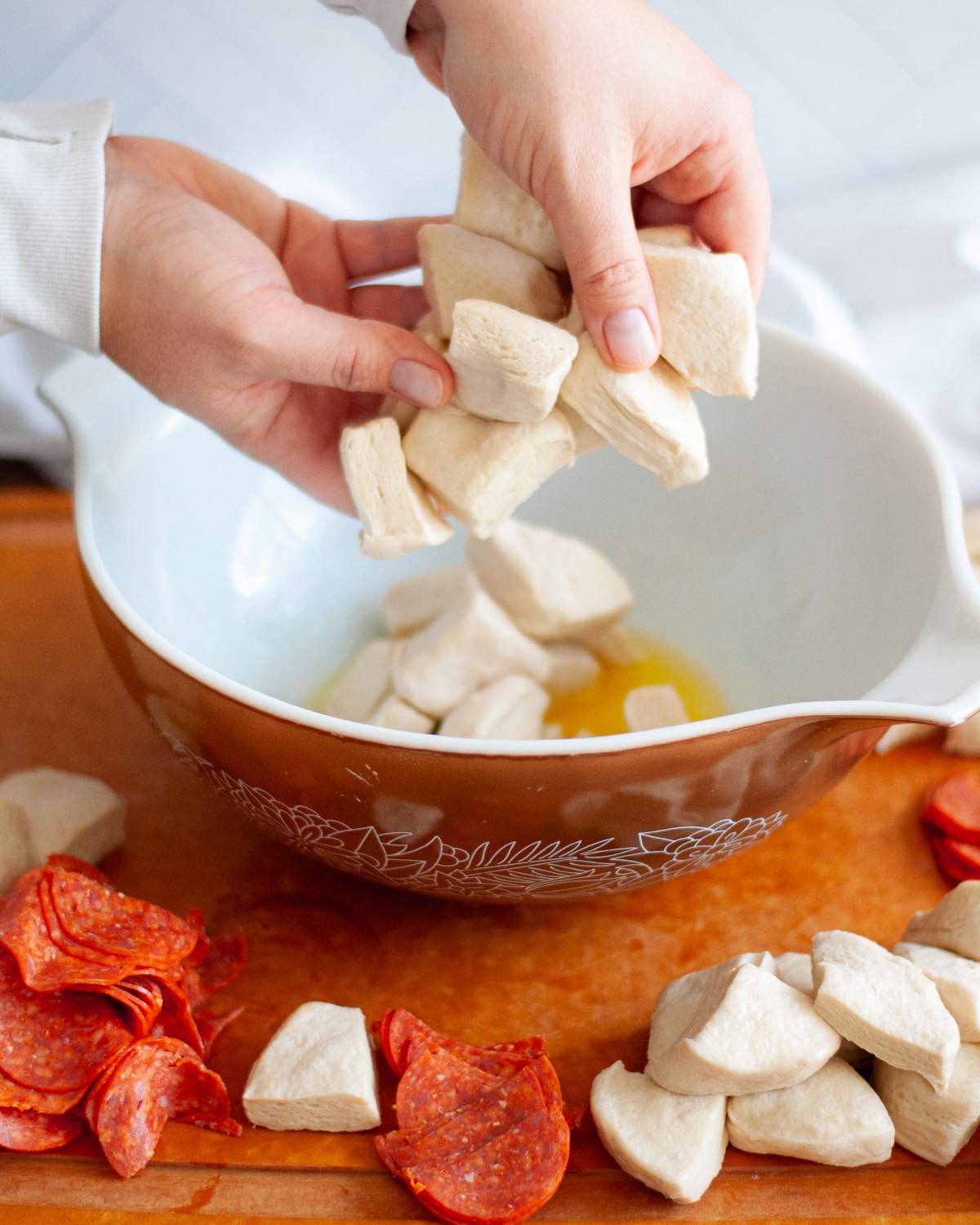 process shot showing how to make pizza monkey bread. here the biscuit pieces are being added into a large mixing bowl with melted butter.