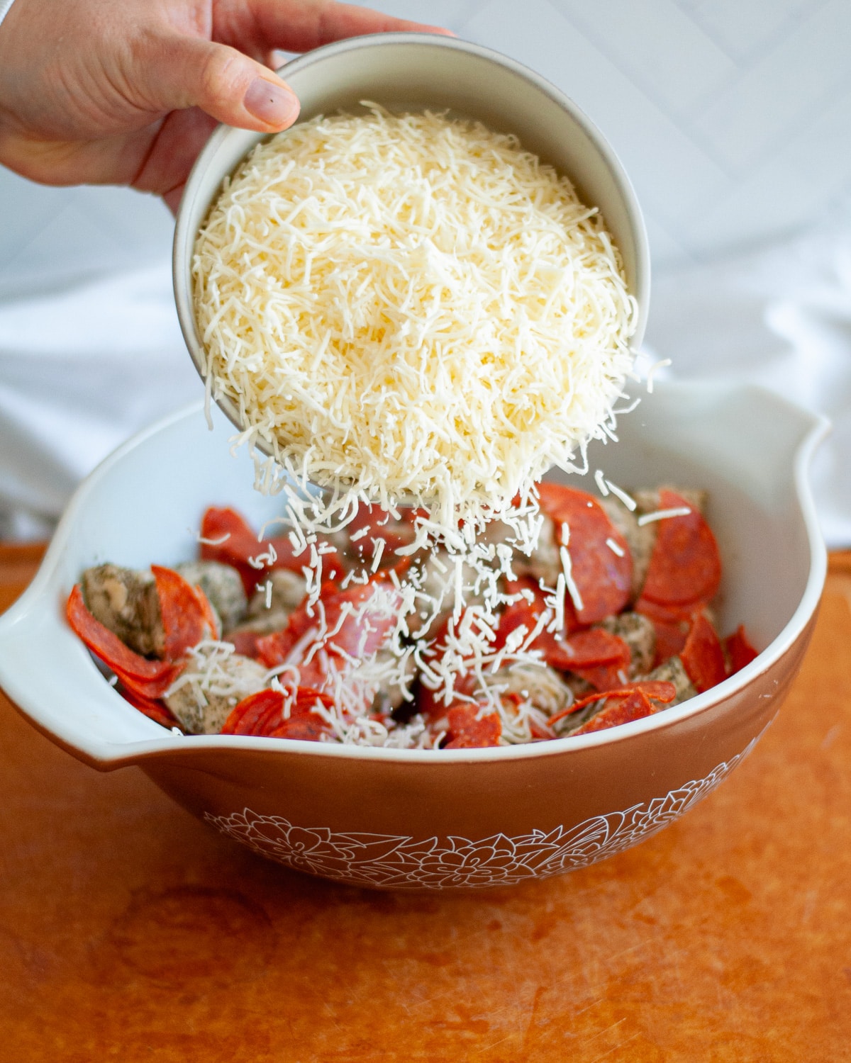 process shot showing how to make pizza monkey bread. here the cheese is being added to the large mixing bowl.