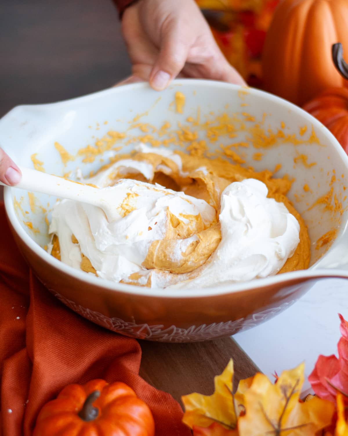 process shot showing how to make pumpkin dip. the thawed cool whip is being gently folded into the rest of the ingredients.