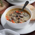 A white bowl filled with wild rice soup, with crusty bread for serving.