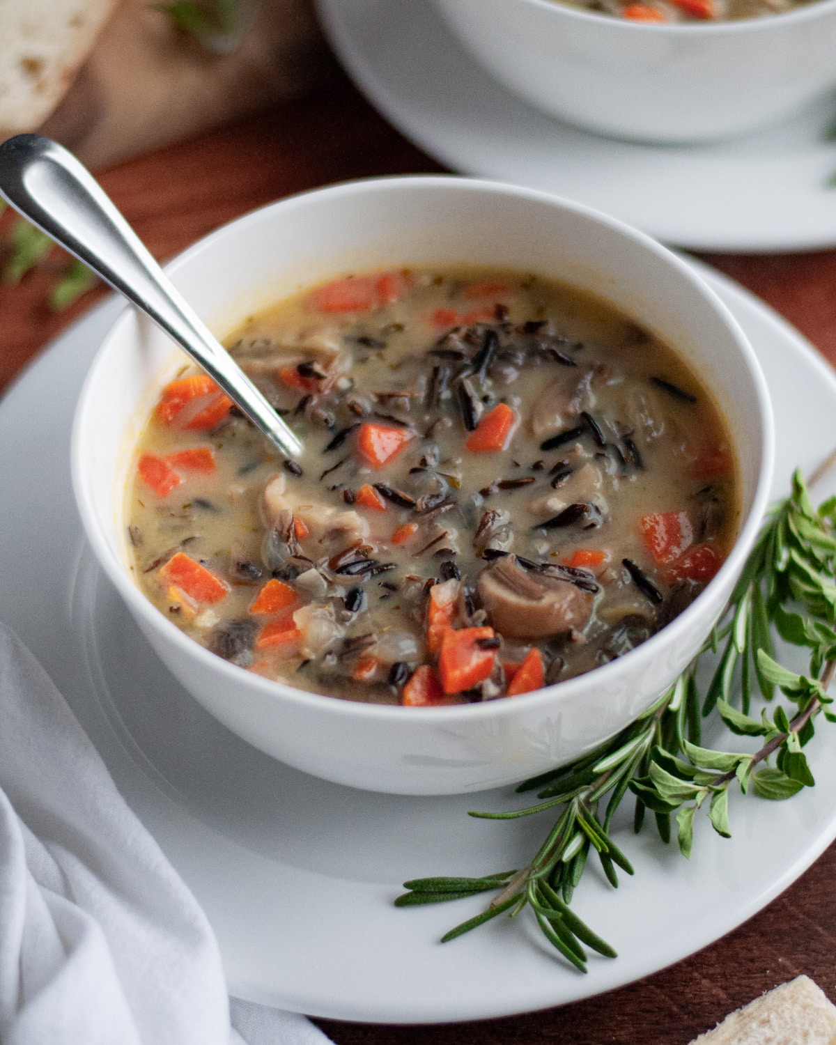 A white bowl filled with wild rice soup with a spoon in it.