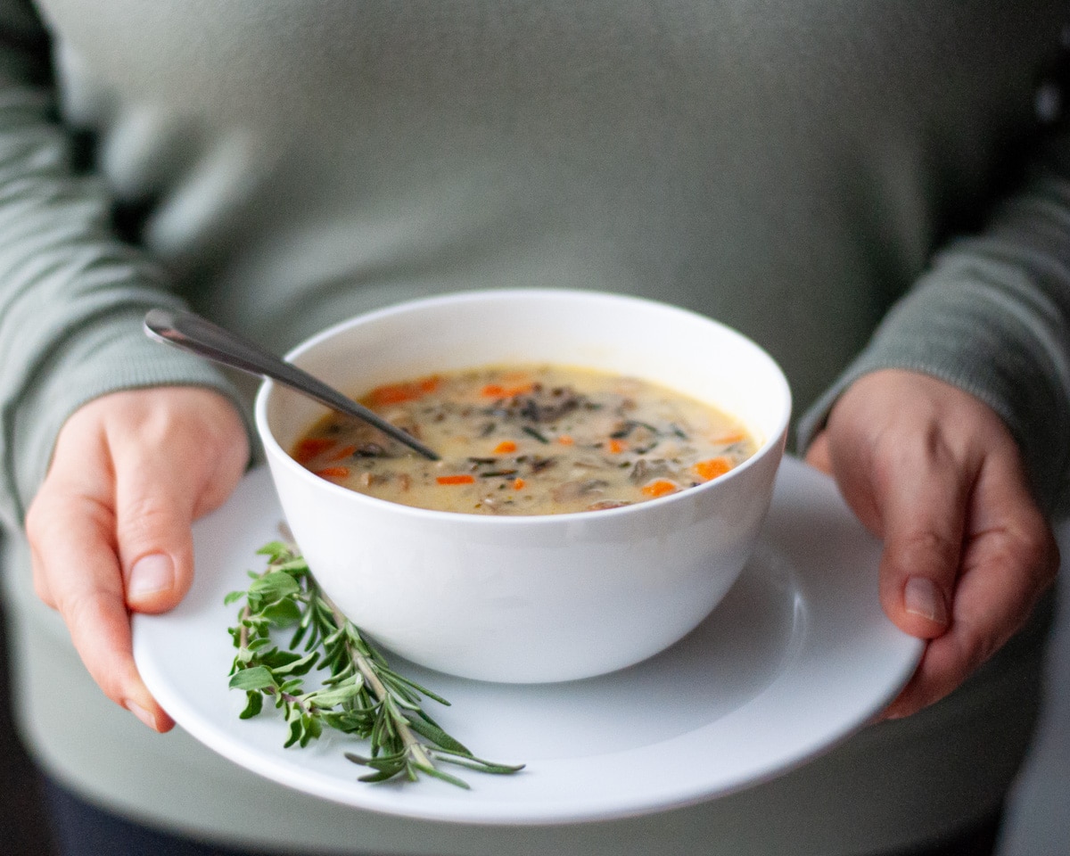 Close of a person holding a plate with a bowl of wild rice soup on it.