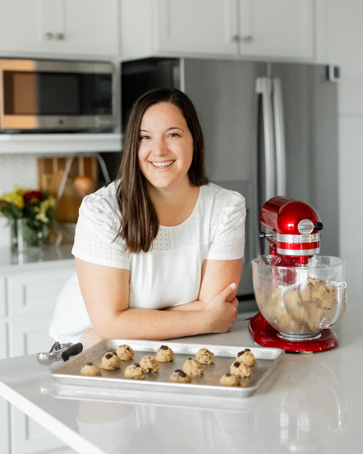 Photo of Meredith, creator of Our Love Language is Food, with a cookie sheet filled with dough balls ready to bake next to a stand mixer with more cookie dough.