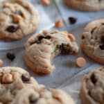 A butterscotch and chocolate chip cookie with a bite out of it that is surrounded by more cookies, chocolate chips, and butterscotch chips.