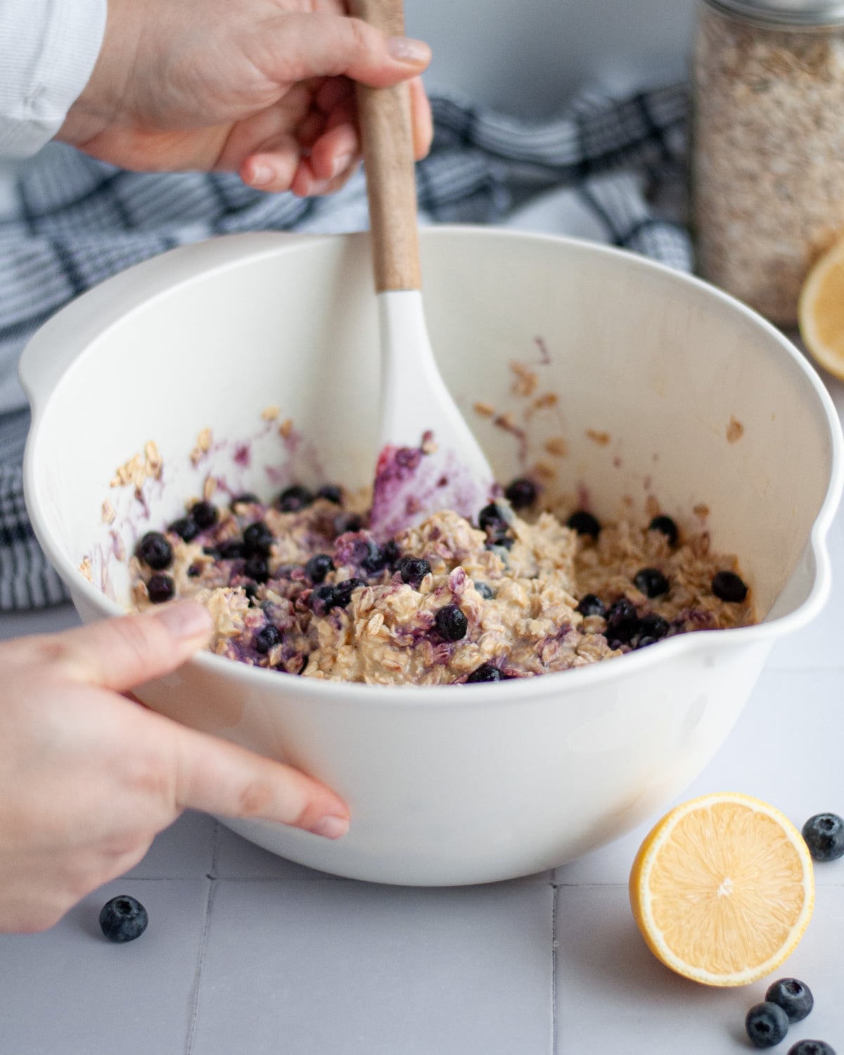 Process shot showing how to make lemon blueberry applesauce baked oatmeal, gently stirring in the frozen blueberries into the oatmeal mixture in a large mixing bowl.
