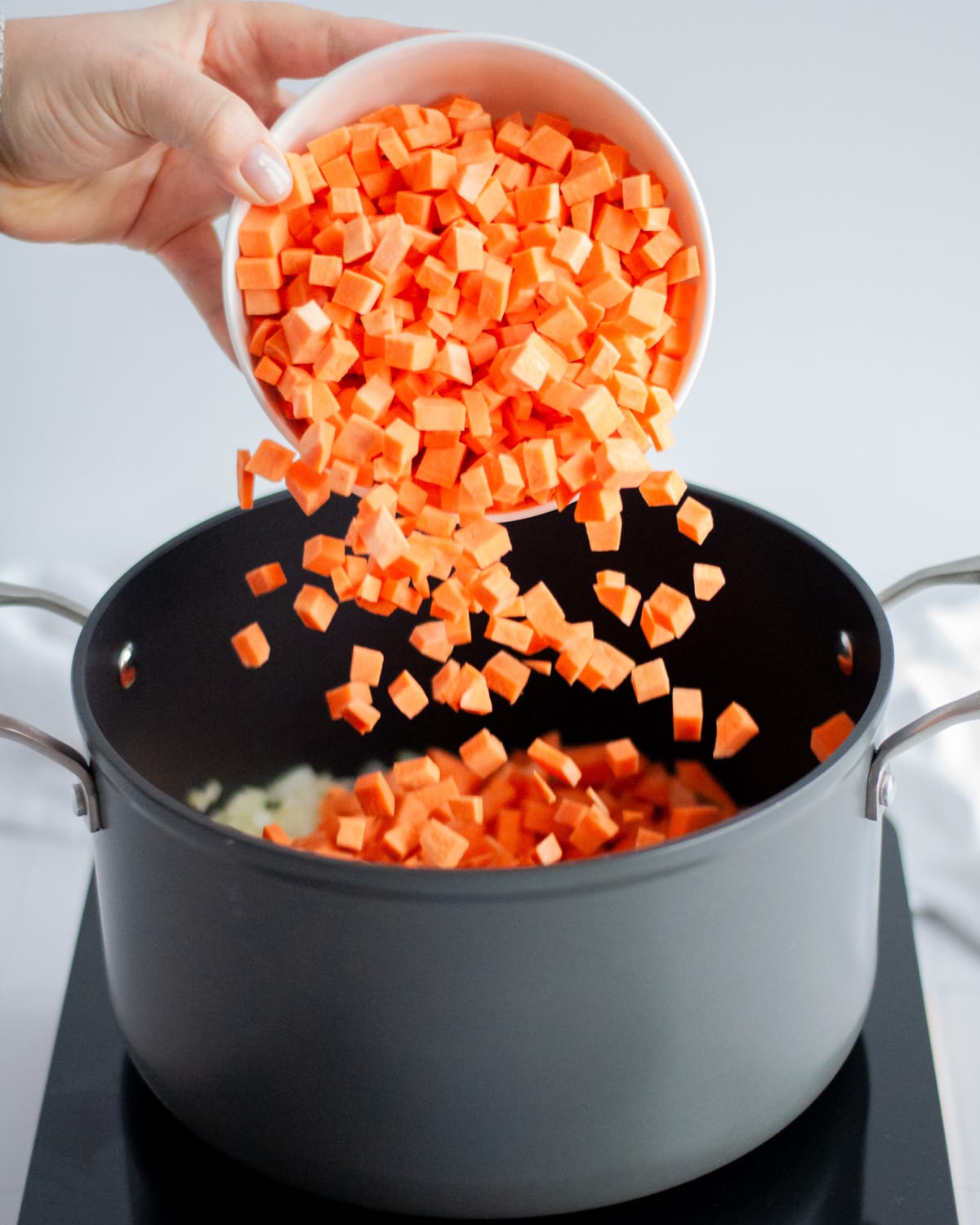 Process shot showing how to make black bean sweet potato chili, showing diced sweet potatoes being added to a large pot.