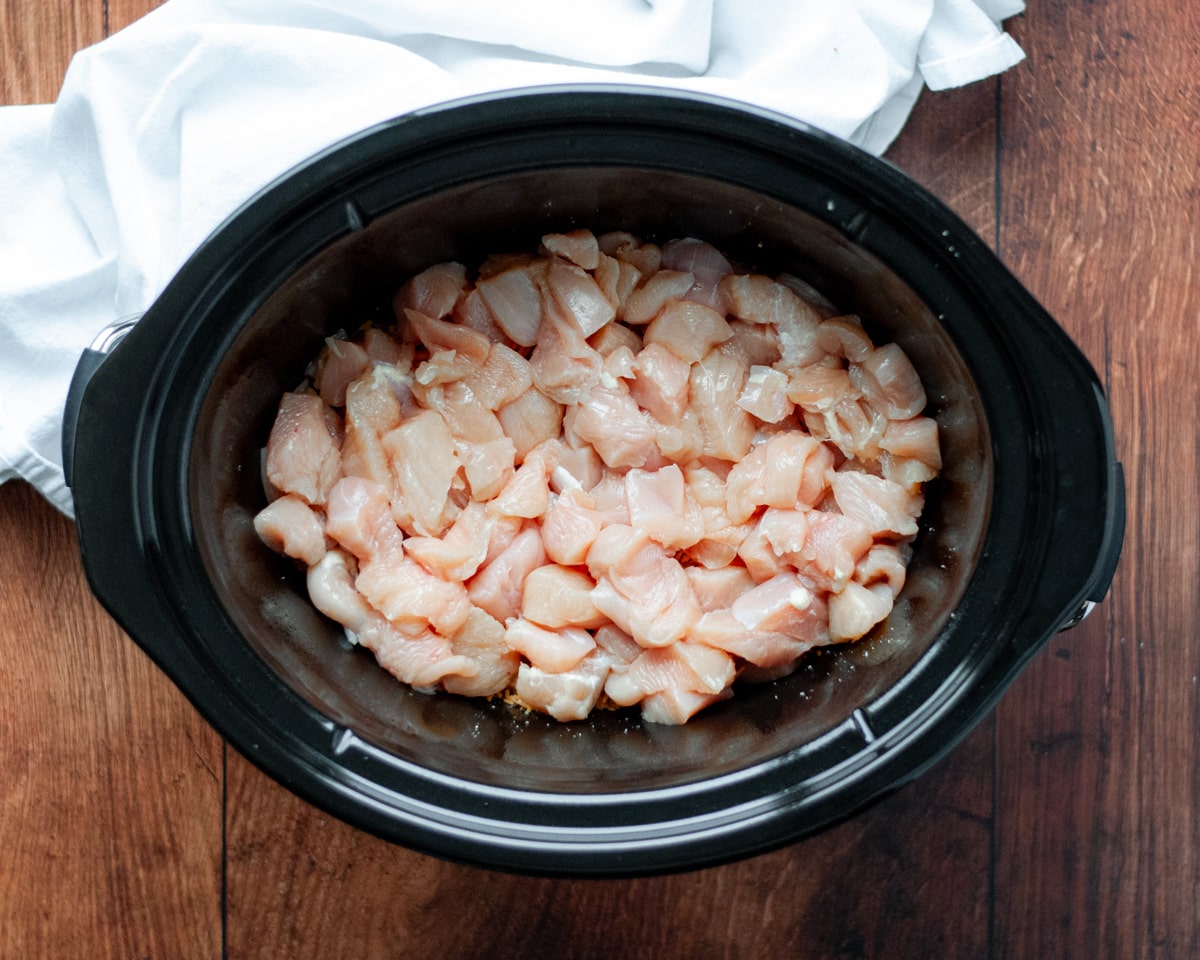 Process shot showing how to make tater tot and chicken casserole in the slow cooker, showing the layer of chicken breast pieces.