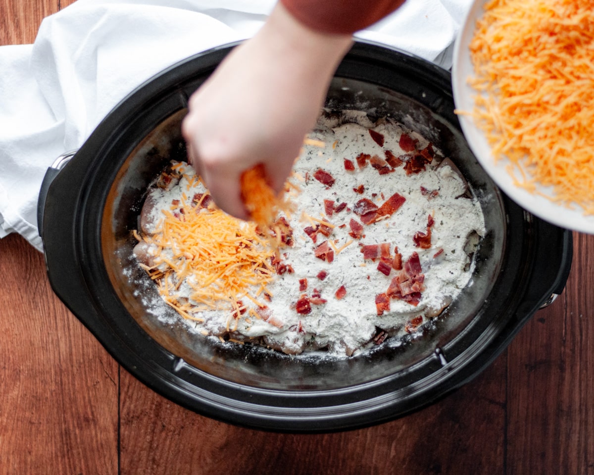 Process shot showing how to make tater tot and chicken casserole in the slow cooker, showing the second layer of bacon and cheese going in.