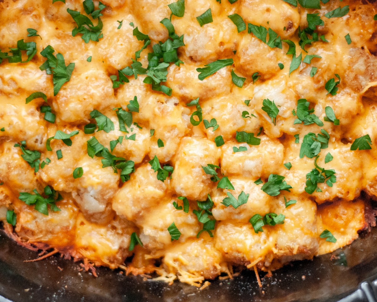 Close up of the ranch bacon chicken and tater tot casserole with fresh herbs sprinkled on top inside the crockpot basin.