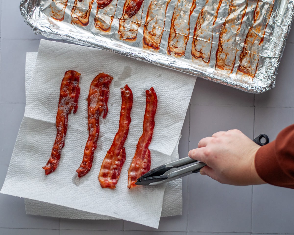 Cooked bacon that has been removed from the lined bacon sheet onto a paper towel lined plate to remove excess grease.