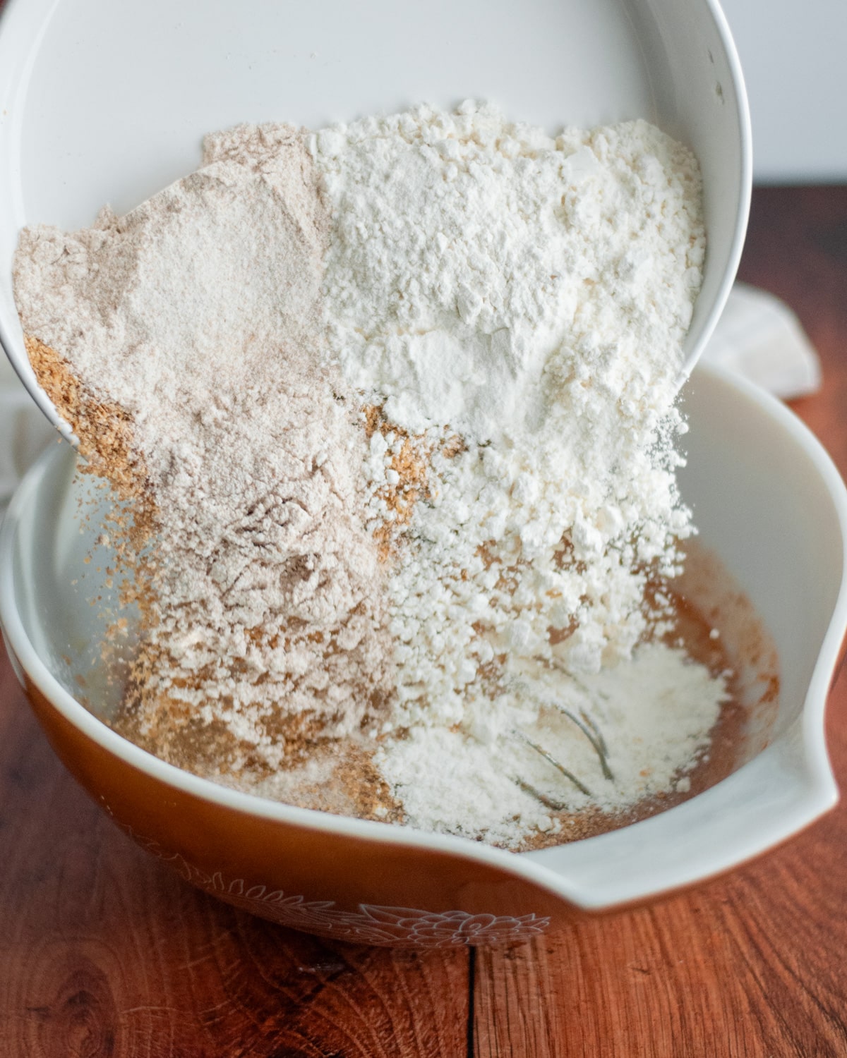 Process shot showing how to make wheat germ muffins; image shows dry ingredients being added to the wet ingredients in a large mixing bowl.