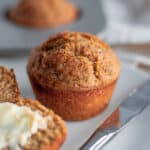 Close up of a full wheat germ muffin on a white serving plate with a buttered muffin in the foreground.