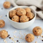 A bowl of peanut butter energy bites surrounded by additional protein balls, oatmeal, and chocolate chips.