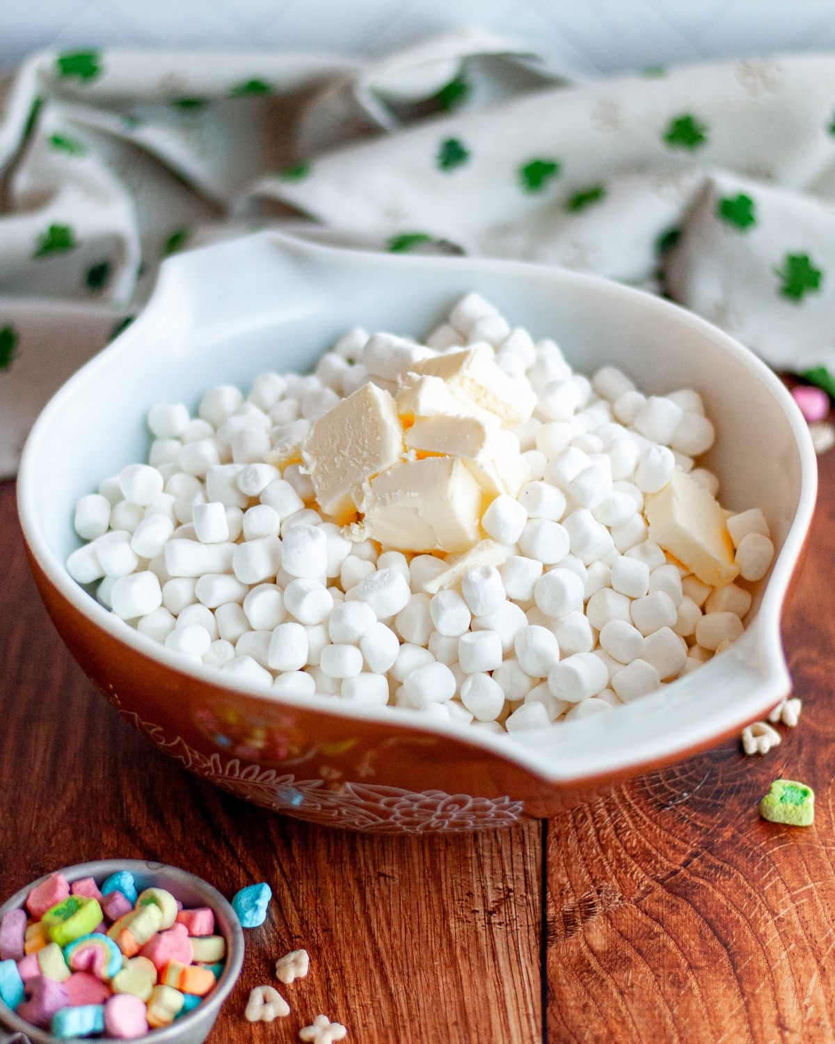 Process shot showing butter added on top of the mini marshmallows in a large bowl.