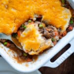 A serving spoon dipped into the baking dish of cottage pie, ready to serve up a scoop.