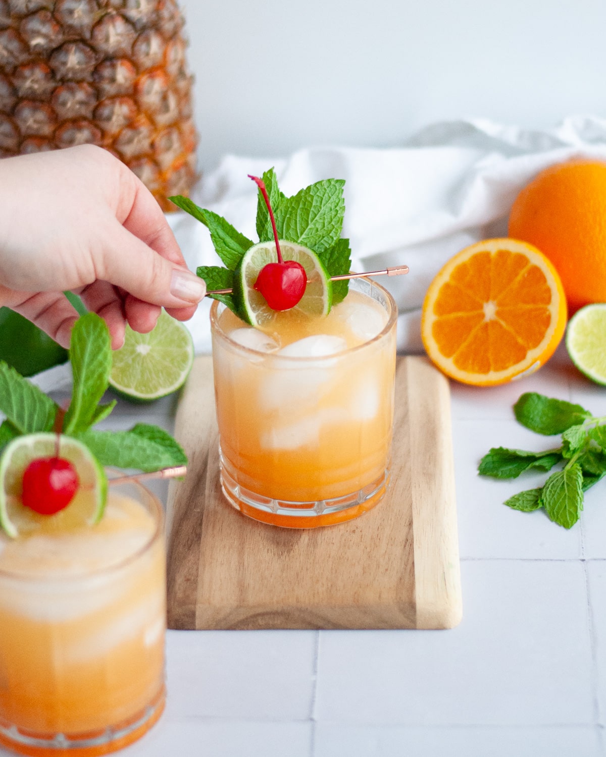 A virgin mai tai being garnished with a mint sprig, lime slice, and maraschino cherry.