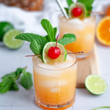 Two virgin mai tai mocktails in lowball glasses garnished with a mint sprig, lime slice, and maraschino cherry.