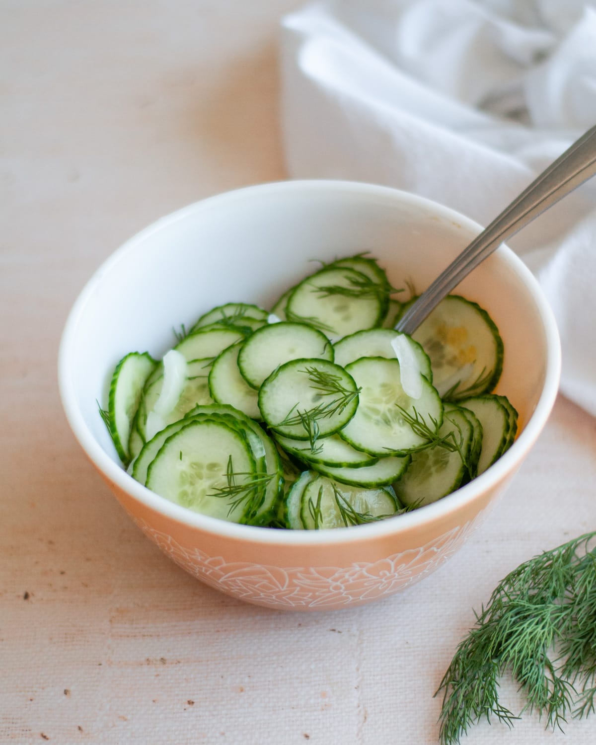 A bowl of old-fashioned cucumber salad with a serving spoon in it.