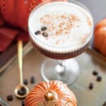 Close up of three coffee beans floated on top of a frothy pumpkin espresso martini with a dash of pumpkin pie spice.