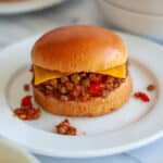 Close up of a lentil sloppy joe sandwich with cheese on a white plate.