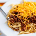Close up of a plate of skyline chili served over spaghetti with cheese on top of it.