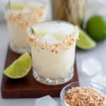 Close up of a coconut lime margarita in a rocks glass rimmed with toasted coconut.