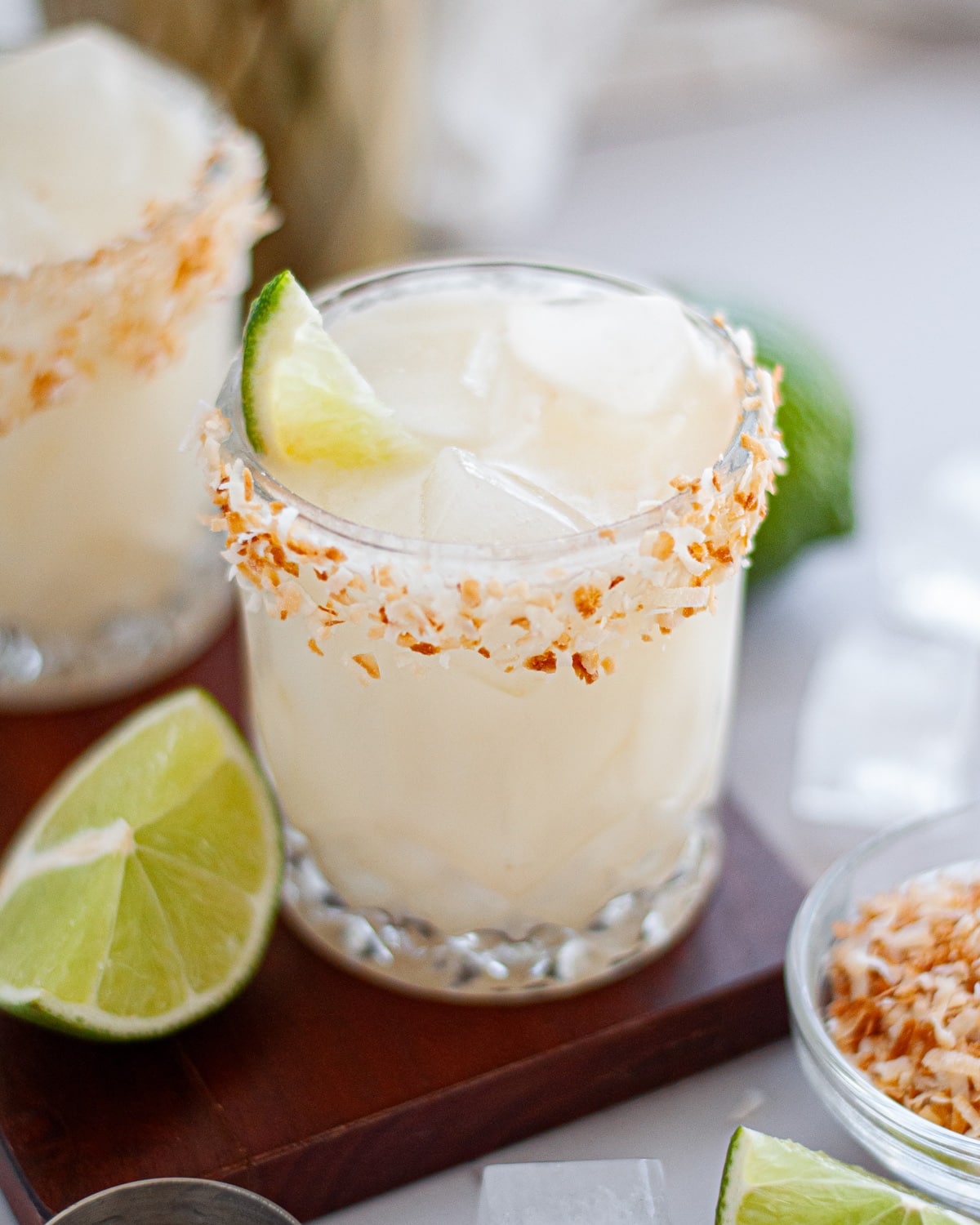Close up of a coconut lime margarita in a rocks glass rimmed with toasted coconut.