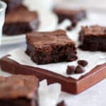 Close up of a cut brownie square sitting on parchment paper and a cutting board.