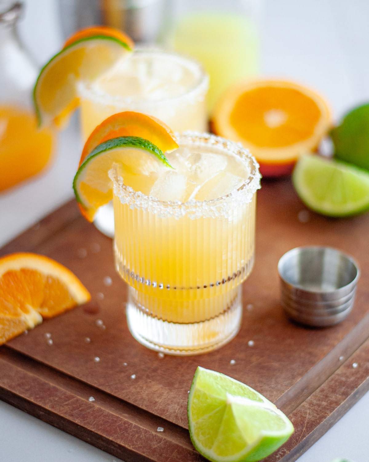 Close up of a skinny margarita in a glass rimmed with salt and garnished with a lime wedge and an orange wedge.