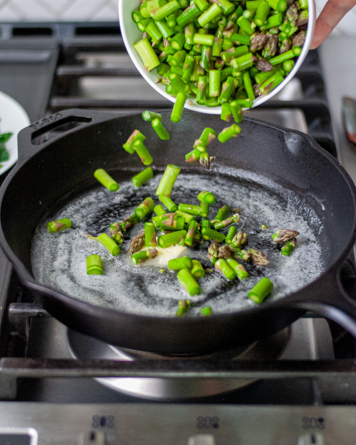 Process shot showing the asparagus pieces being added to the cast iron skillet.