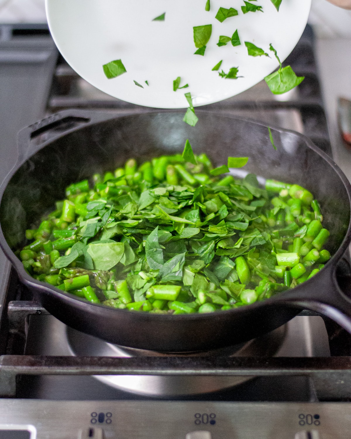 Process shot showing the spinach being added to the cast iron skillet.