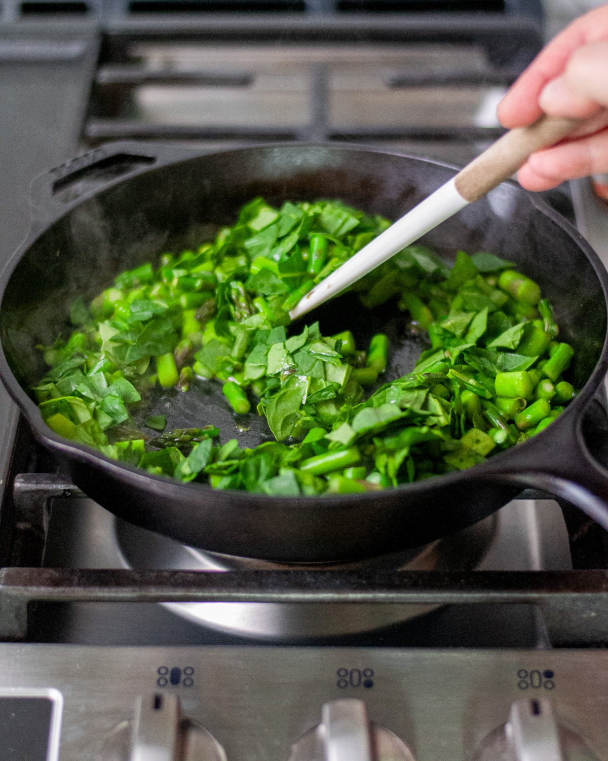 Process shot showing the spinach being stirred in with the asparagus.