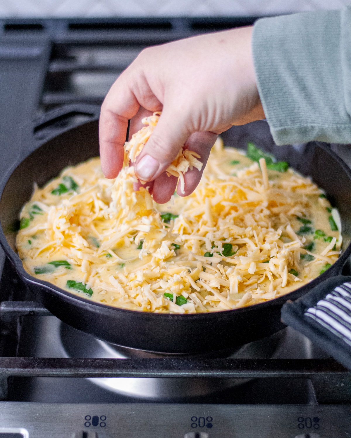 Process shot showing the grated cheese being sprinkled over the egg mixture.