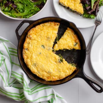 Top down view of the frittata in the cast iron skillet, with a slice removed.