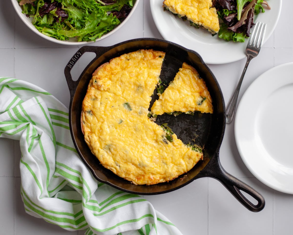 Top down view of the frittata in the cast iron skillet, with a slice removed.