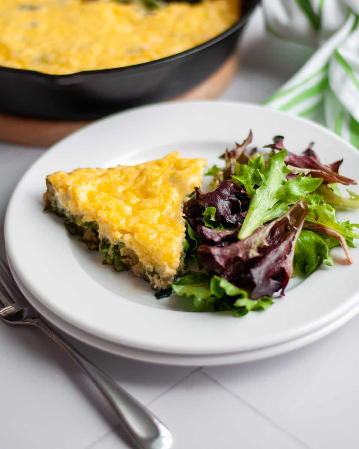A slice of asparagus frittata on a plate with a side salad.