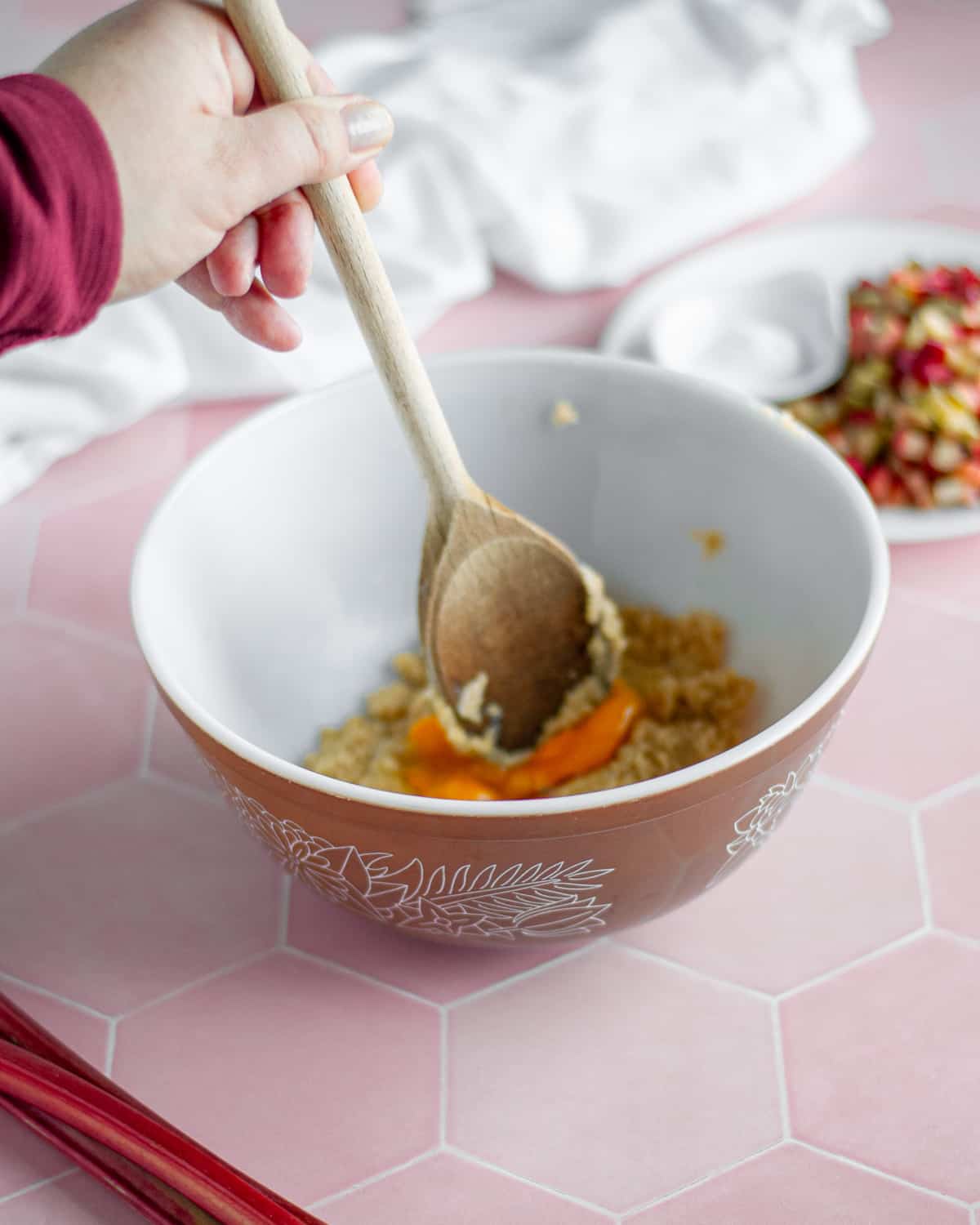 Process shot showing the egg yolk being broken up with a wooden spoon.