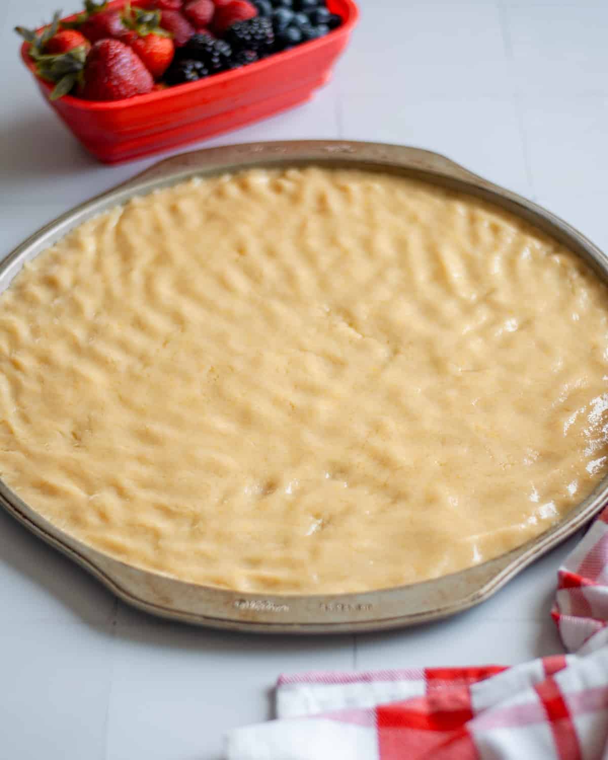 Process shot showing the sugar cookie crust dough pressed into an even layer in a pizza tin.