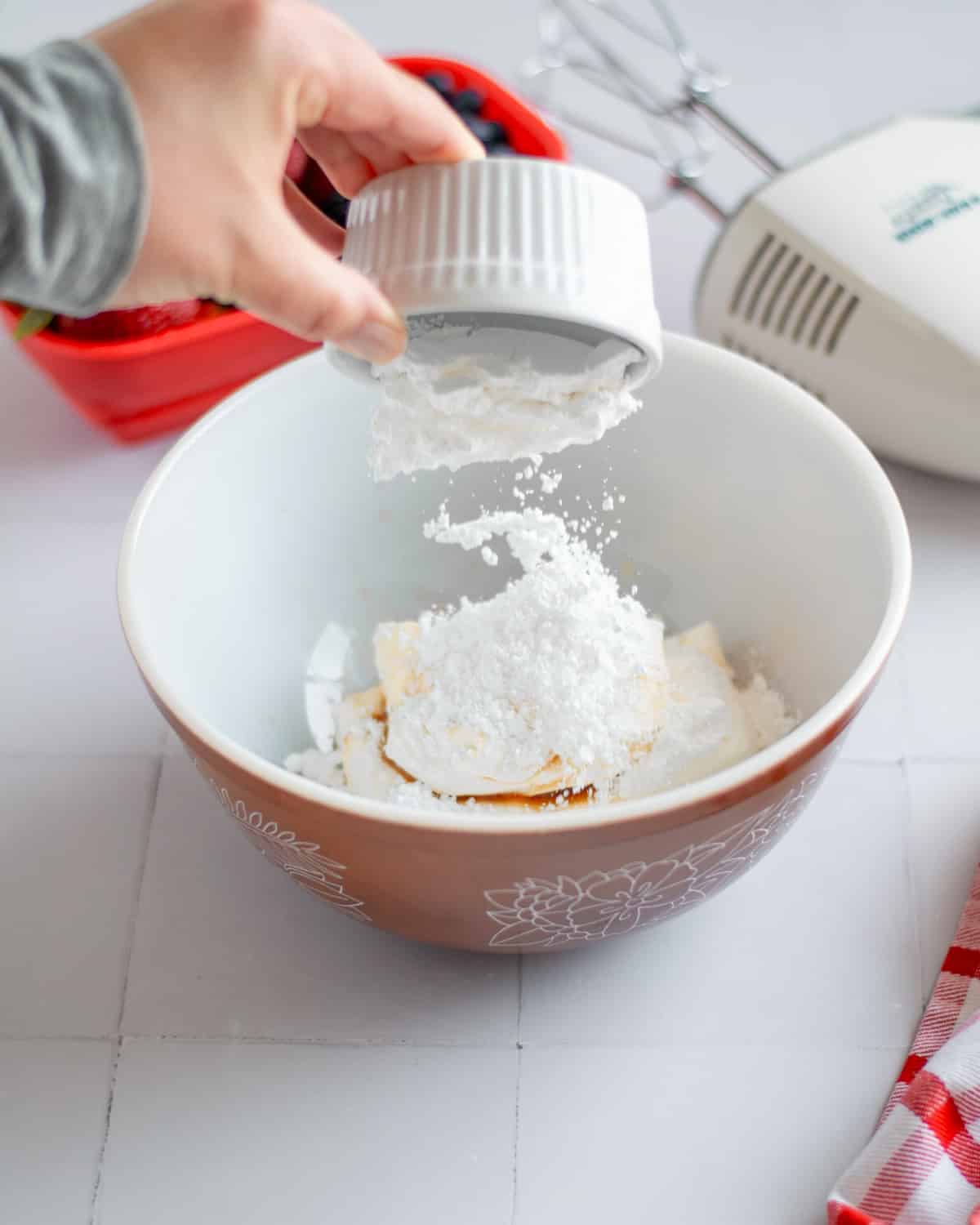 Process shot showing the fruit pizza frosting ingredients being added to a medium mixing bowl.