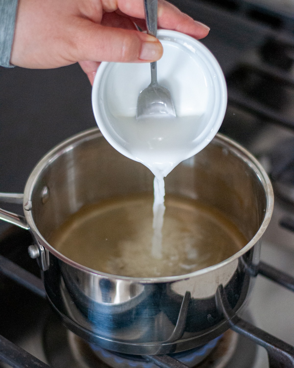 Process shot showing the cornstarch slurry being added to the other fruit pizza glaze ingredients being in a saucepan.