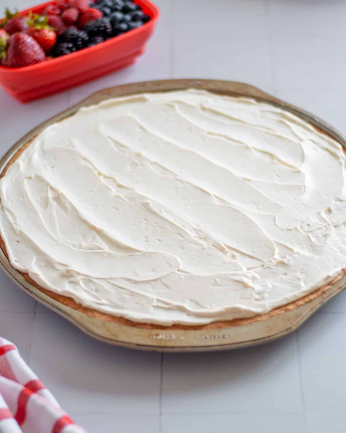 Process shot showing the fruit pizza frosting spread into an even layer over the cookie crust.