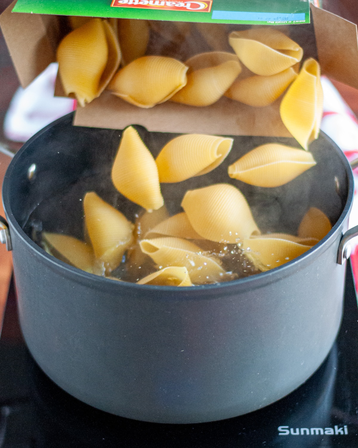 Process shot showing the dry pasta being added to boiling water.