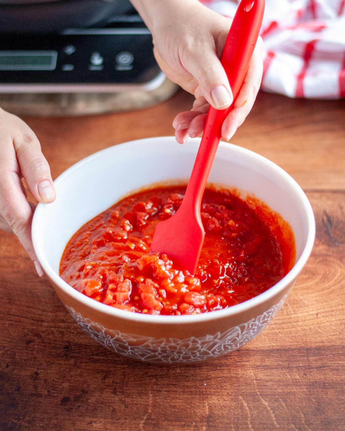Process shot showing the pasta sauce and diced tomatoes being mixed together in a small bowl.
