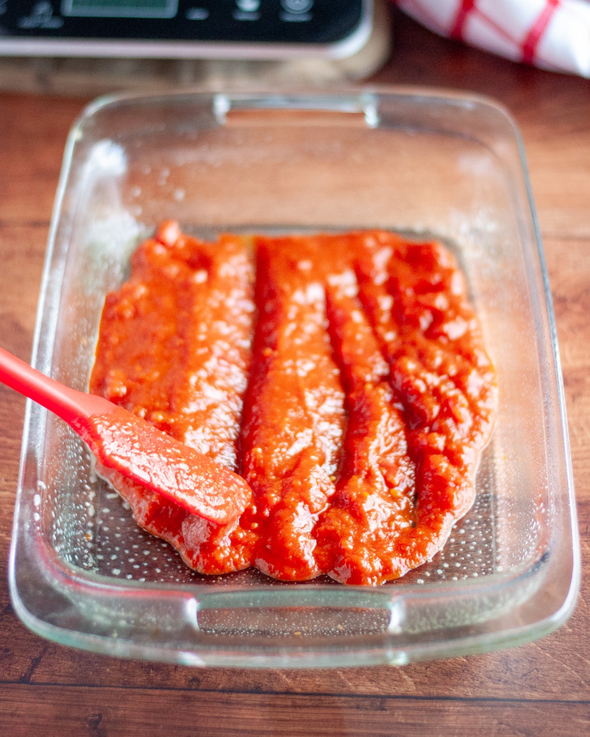Process shot showing the sauce mixture being spread into a thin layer in a greased 9x13 pan to coat the bottom.