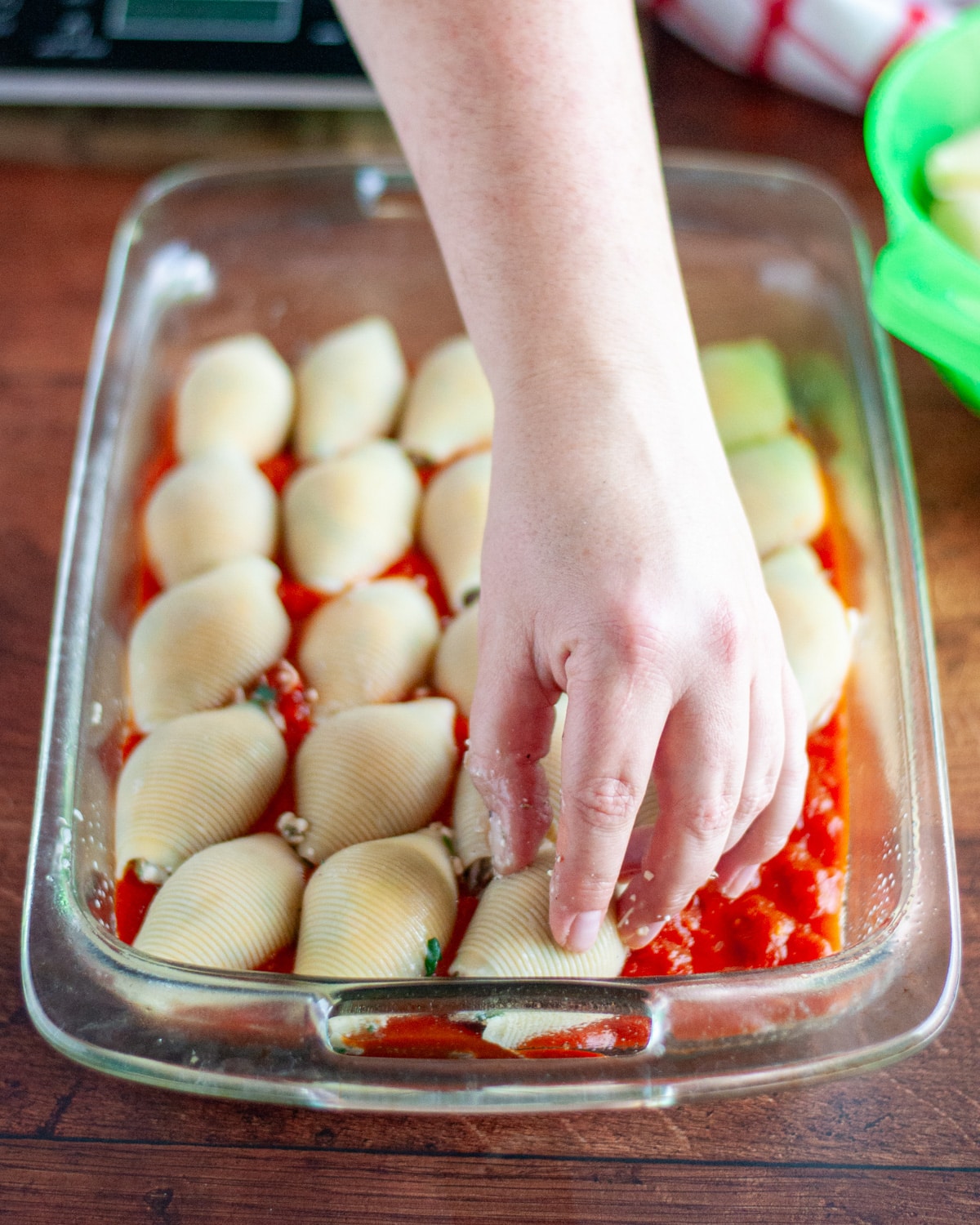 Process shot showing the stuffed shells being place face-down into the sauce covered pan.