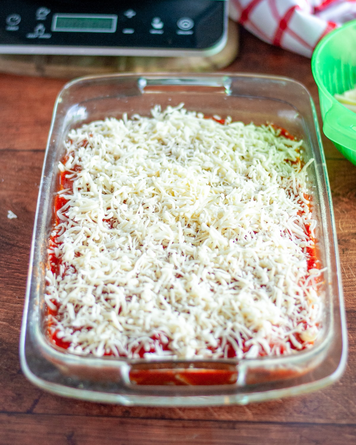 Process shot showing the cheese sprinkled over the sauce covered shells in the pan.